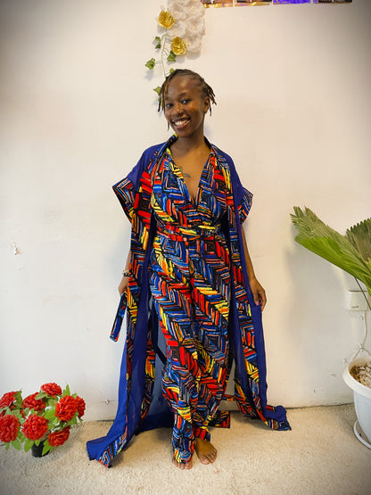 Woman wearing a colorful patterned outfit standing indoors with a white wall and plants in the background.