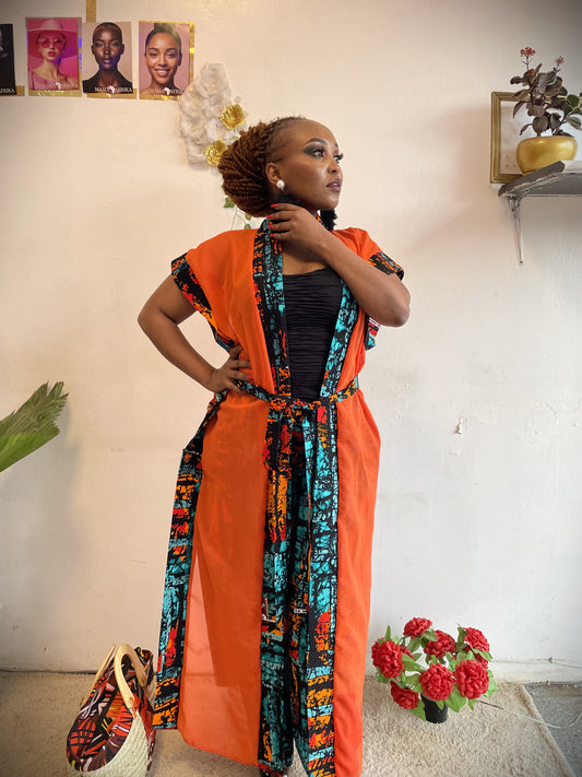 Woman wearing an orange and colorful patterned outfit with a white wall background