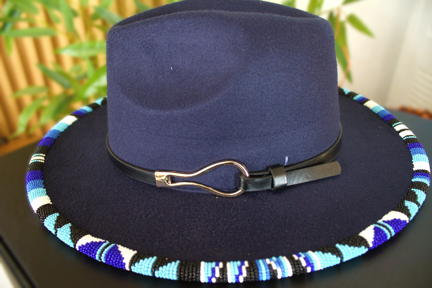 Navy blue fedora hat with a colorful beaded band on a dark surface.