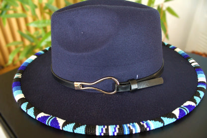 Navy blue fedora hat with a colorful beaded band on a dark surface.