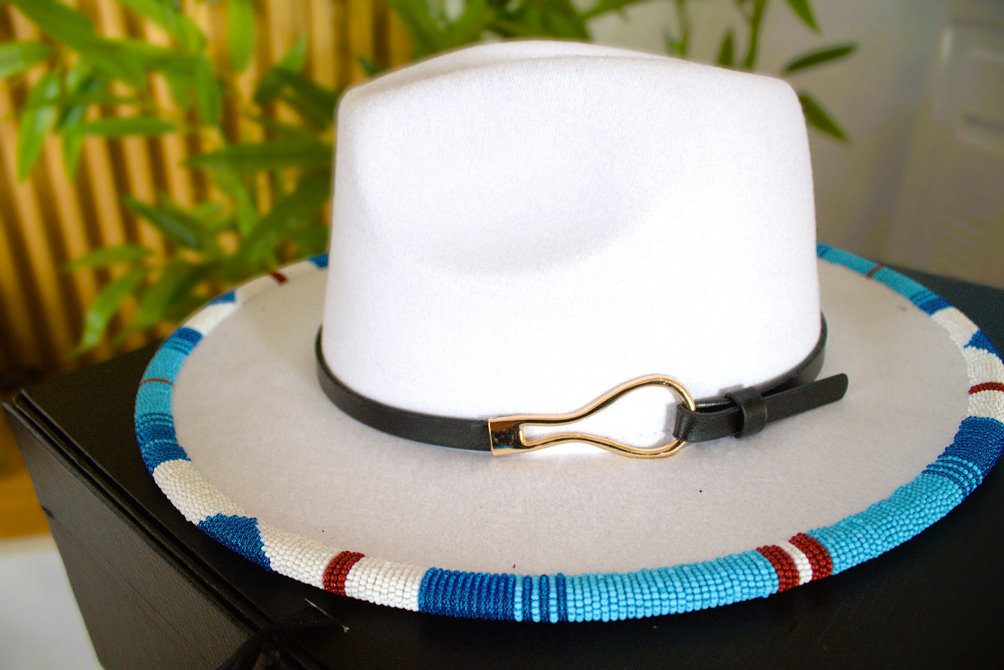 White fedora hat with a colorful band and black strap on a dark surface.