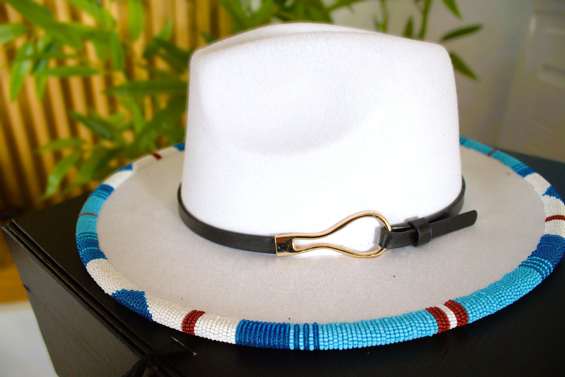 White fedora hat with a colorful band and black strap on a dark surface.