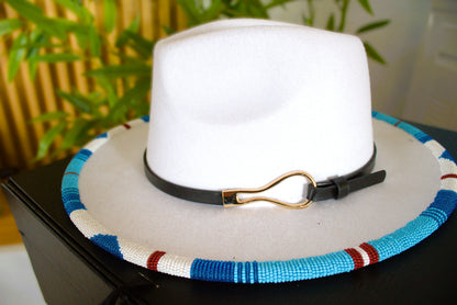 White fedora hat with a colorful band and black strap on a dark surface.